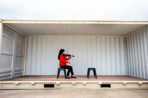 Rayna Yun Chou gives a sense of what’s expected in “Concert for One” event. (Photo: Robert Torres) Image of musician playing violin inside of a large shipping container